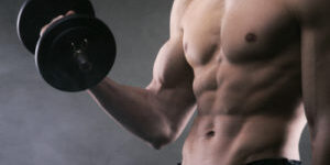 Muscular male athlete is training by lifting dumbbells