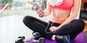 Крупним планом молода жінка-спортсменка, яка сидить на килимку та використовує мобільний телефон у спортзалі, 582510 відредаговано
