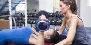 Female-trainer-helping-female-client-lifting-weights-in-gym