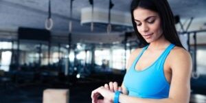Happy-young-woman-using-activity-tracker-in-fitness-gym